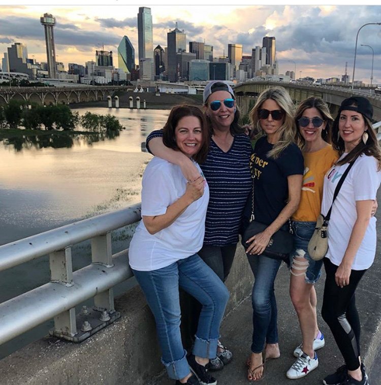 Women standing on bridge with Dallas skyline in the back.