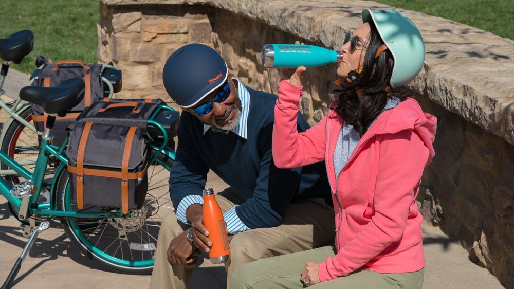 Couple sitting and drinking water while wearing Thousand bike helmets.