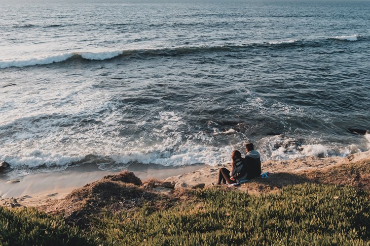 Couple sitting on the beach looking out at the sunset.